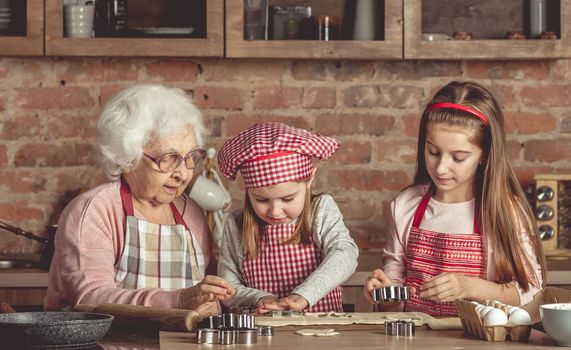 Two little granddaughters help granny to bake cookies at the rustic kitchen