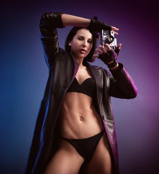 the brunette photographer girl in underwear and a leather raincoat poses in a photo studio with a camera