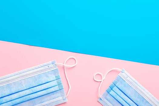 Medical face mask on pink and blue paper background with copy space top view