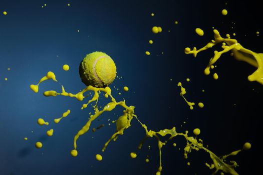 A tennis ball and splashes of yellow paint form a mantis figurine on a blue background.