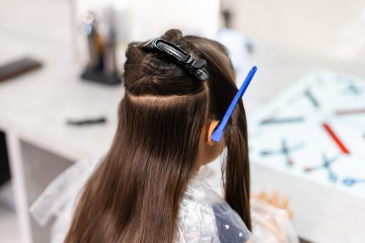 Portrait of pretty little girl seating at table with accessories in a hairdressing salon