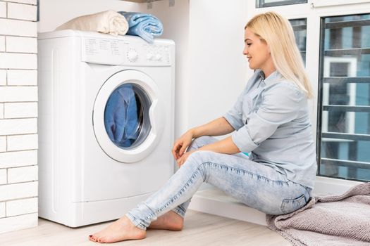 A young housewife with washing machine and clothes. Washing day.