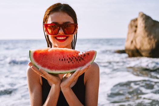 cheerful woman in sunglasses eating watermelon by the ocean. High quality photo