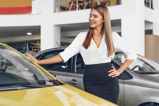 Young woman checking out a new car she is going to buy in car salon