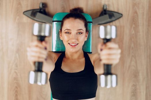 Young brunette sporty woman exercising with dumbbell in a gym close up