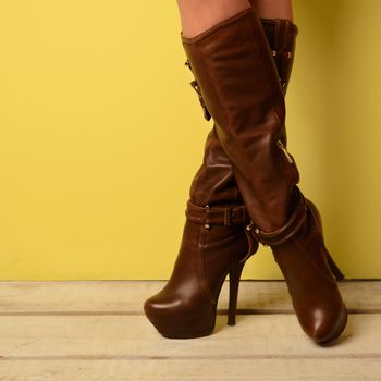 girl in brown spring boots stands cross-legged on a white wooden floor.