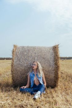 Beautiful girl villager posing in jeans near a bale of hay in a field