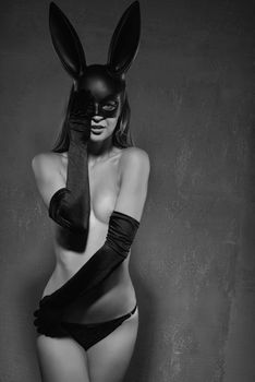 Black and white photo of beautiful woman in black panties, satin gloves and a plastic rabbit mask is covering one eye with her hand