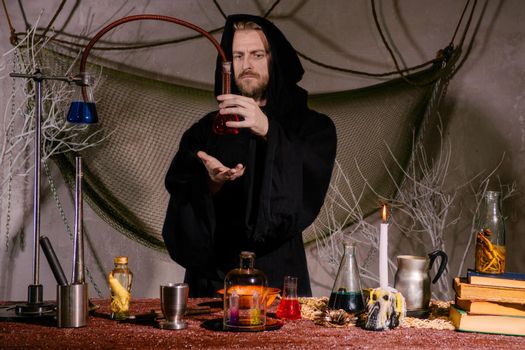 The medieval alchemist scientist conducts a ritual in his laboratory.. Halloween concept. The bearded magician in the mantle