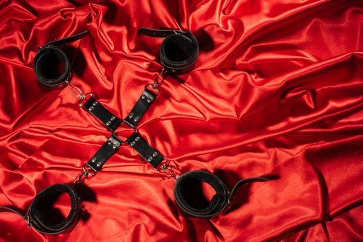 Top view of bdsm outfit. Bondage crossed on the red linen. Adult sex games. Kinky lifestyle. - image