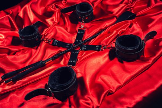 Top view of bdsm outfit. Bondage and spank on the red linen. Adult sex games. Kinky lifestyle. - image