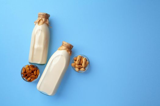 Bottles of vegan non dairy milk with various nuts on blue background, top view