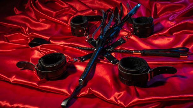 Top view of bdsm outfit. Bondage and whip crossed spank on the red linen. Adult sex games. Kinky lifestyle. - image