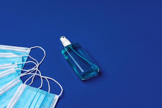 Pile of medical face masks with hand sanitizer on blue background close up
