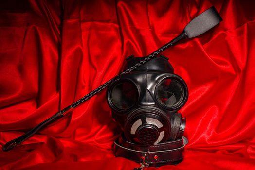 Close up bdsm outfit. Bondage, kinky adult sex games, kink and BDSM lifestyle concept with gas mask, whip, collar on red silk with copy space.