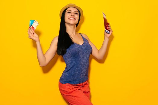 Young smiling excited woman student holding passport boarding pass ticket and credit card isolated on yellow background. Air travel flight - Image