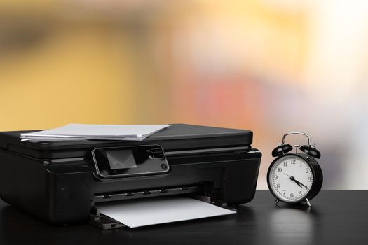 Compact laser printer on black desk against blurred background, close up