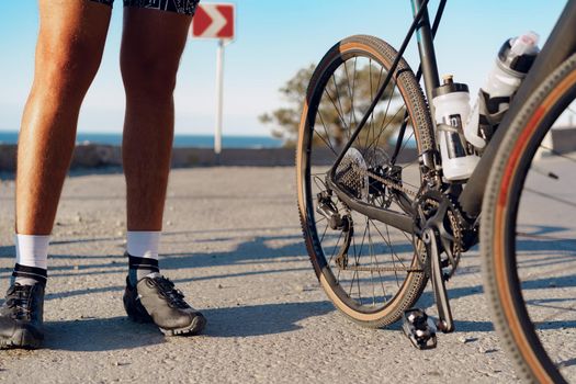 Cyclist man feet and bike wheel on coastal road close up