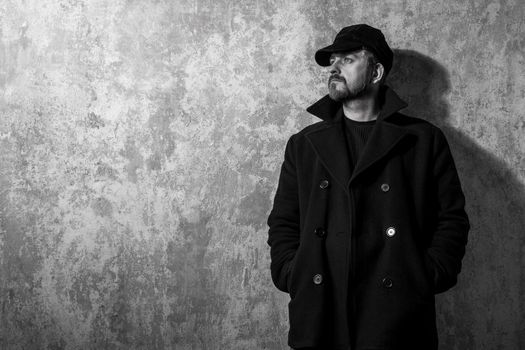 man in vintage cap and coat standing near old wall. black and white photo