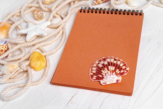 Close up photo of brown notepad with sea shells on wooden planks closeup, copy space