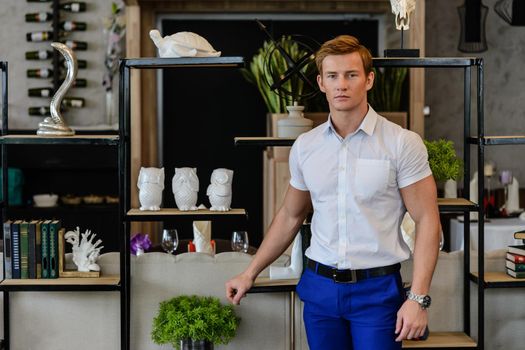 Young sporty man in white shirt and blue pants standing at home near books