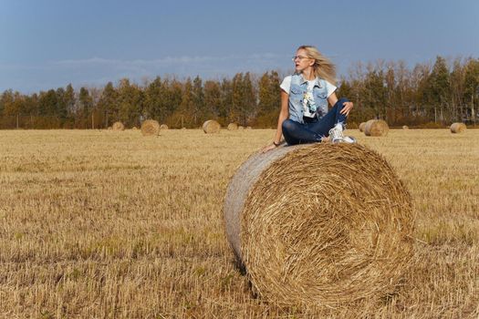Beautiful girl villager posing in jeans on a bale of hay in a field