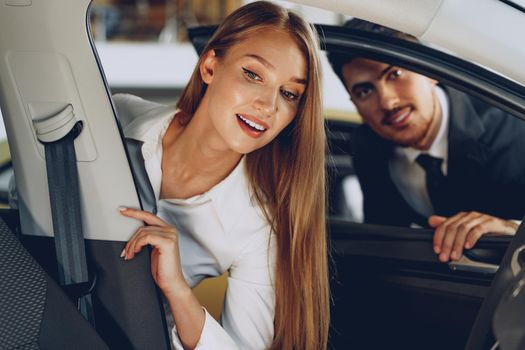 Man car dealer showing a woman buyer a new car in car salon