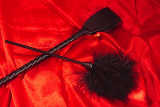 Bondage, kinky adult sex games, kink and BDSM lifestyle concept with a whip, feather stick on red silk with copy space