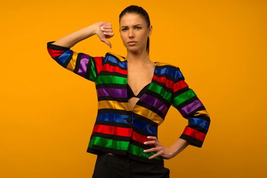 Young lesbian girl and an LGBT community representative posing in a flag coloring jacket LGBTQ shows thumb down - image