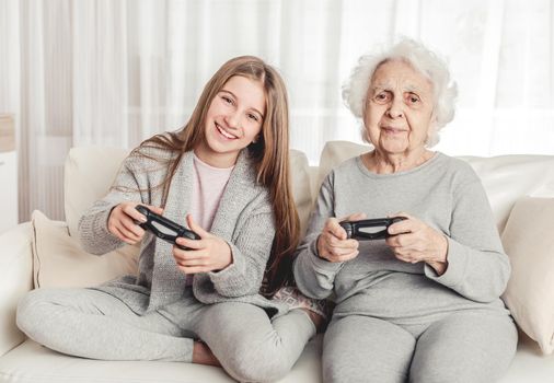 Grandmother with granddaughter playing games together with gamepads