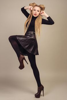 Portrait of a beautiful young girl with two ponytails,takes a step to the side raising his hands to his face. Isolated on gray background.