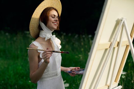 Woman in white dress paints a picture on nature easel. High quality photo