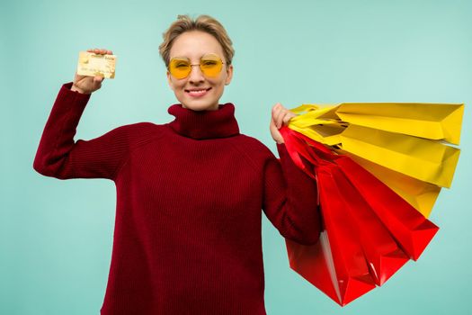 Image of a beautiful happy young blonde woman posing isolated over blue wall background holding shopping bags and credit card. Black Friday Holiday Concept. Sale