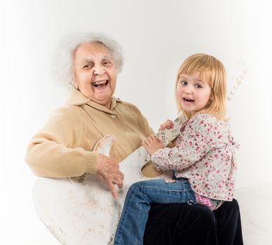 little girl on geatgrandmother knees having fun with quitar
