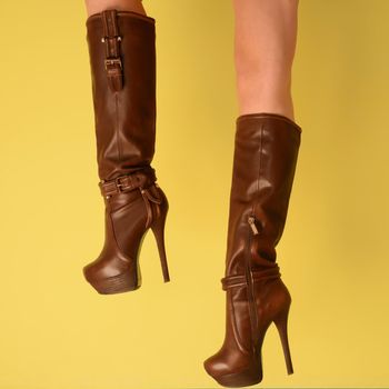 female legs in fashionable leather brown boots on a yellow background