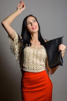 Young fashionable woman in a red skirt with black bag standing smiling holding up one hand to the top