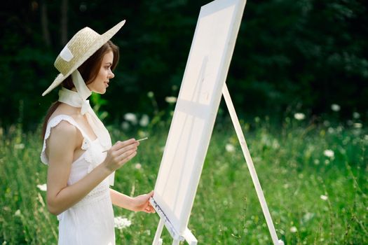 Woman in white dress in nature paints a picture of a landscape hobby. High quality photo