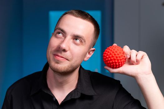 Portrait of a professional young caucasian male masseur in a dark uniform holding a massage ball in his hand for self-massage myofasceal. looking at the camera