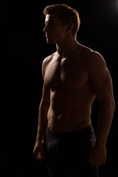 Male fitness model showing muscles in studio with a black background