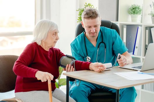 Doctor measuring blood pressure of elderly patient using tonometer during appointment in clinic