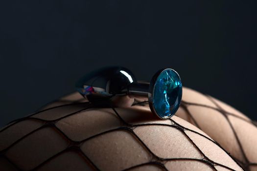 Close-up of anal plug sexy device with blue crystal on the female ass in pantyhose in the fishnet. Adult sex game