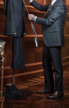 Unrecognizable tailor man measuring suit on dummy with tape-measure.