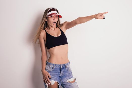 Mischievous girl in a red cap and jeans sports top amazement points a finger to the side