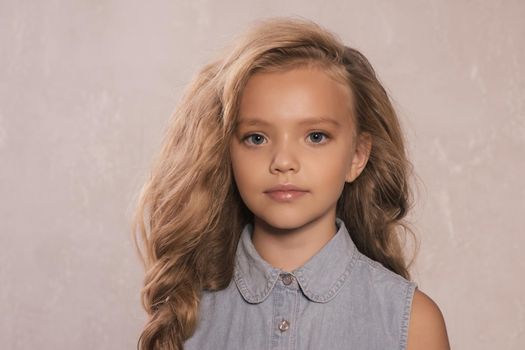 portrait of cute little 8-9 year old girl with blonde hair, wearing jeans jacket, standing against gray background