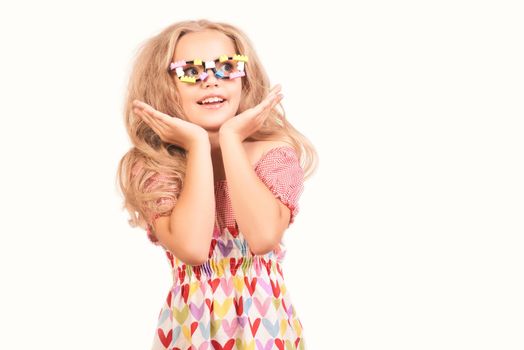 Little cute blonde girl in dress with hearts and glasses looks up side opening mouth in surprise seeing