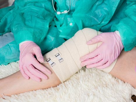 The doctor puts an elastic bandage on the patient's knee. Joint replacement surgery