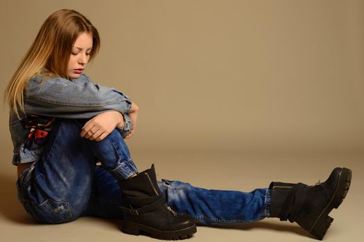 sad teenage girl sitting on the floor of jeans, jacket, shoes . isolated on gray background