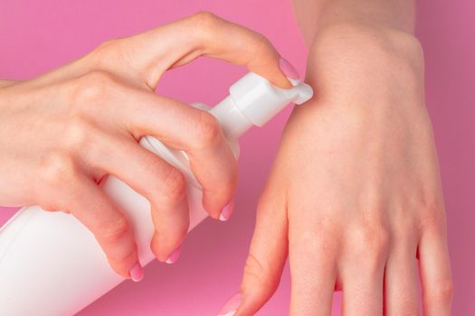 Female hand holding skincare product bottle on pink background