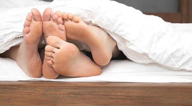 close up feet of a couple under the white sheets blanket in bed, sex hugging and partner valentines concept sexy and romantic