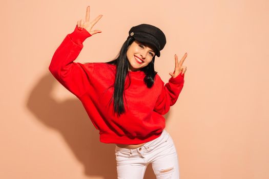 Young smiling girl wearing black cap and red hoodie over isolated background looking to the camera showing fingers doing victory sign. Number two.